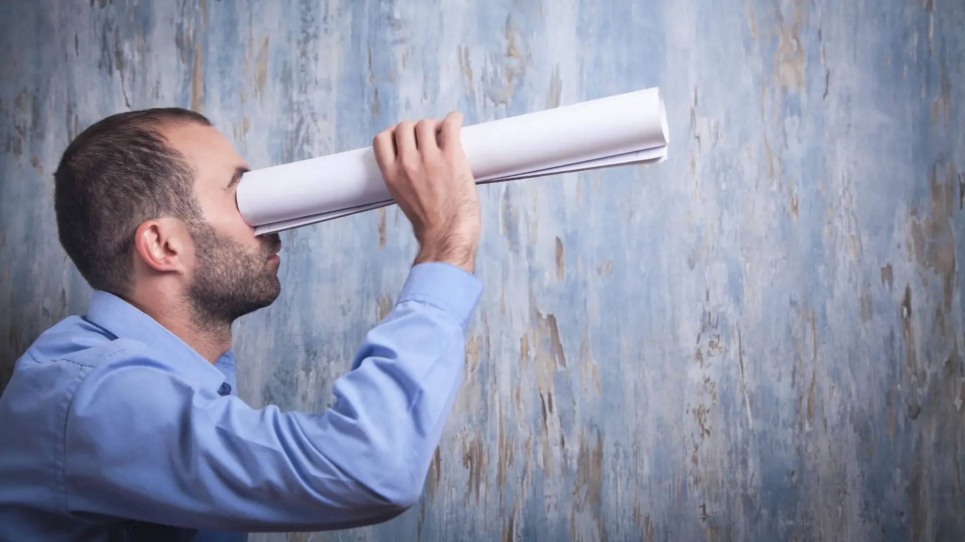 Man looking through a rolled piece of paper
